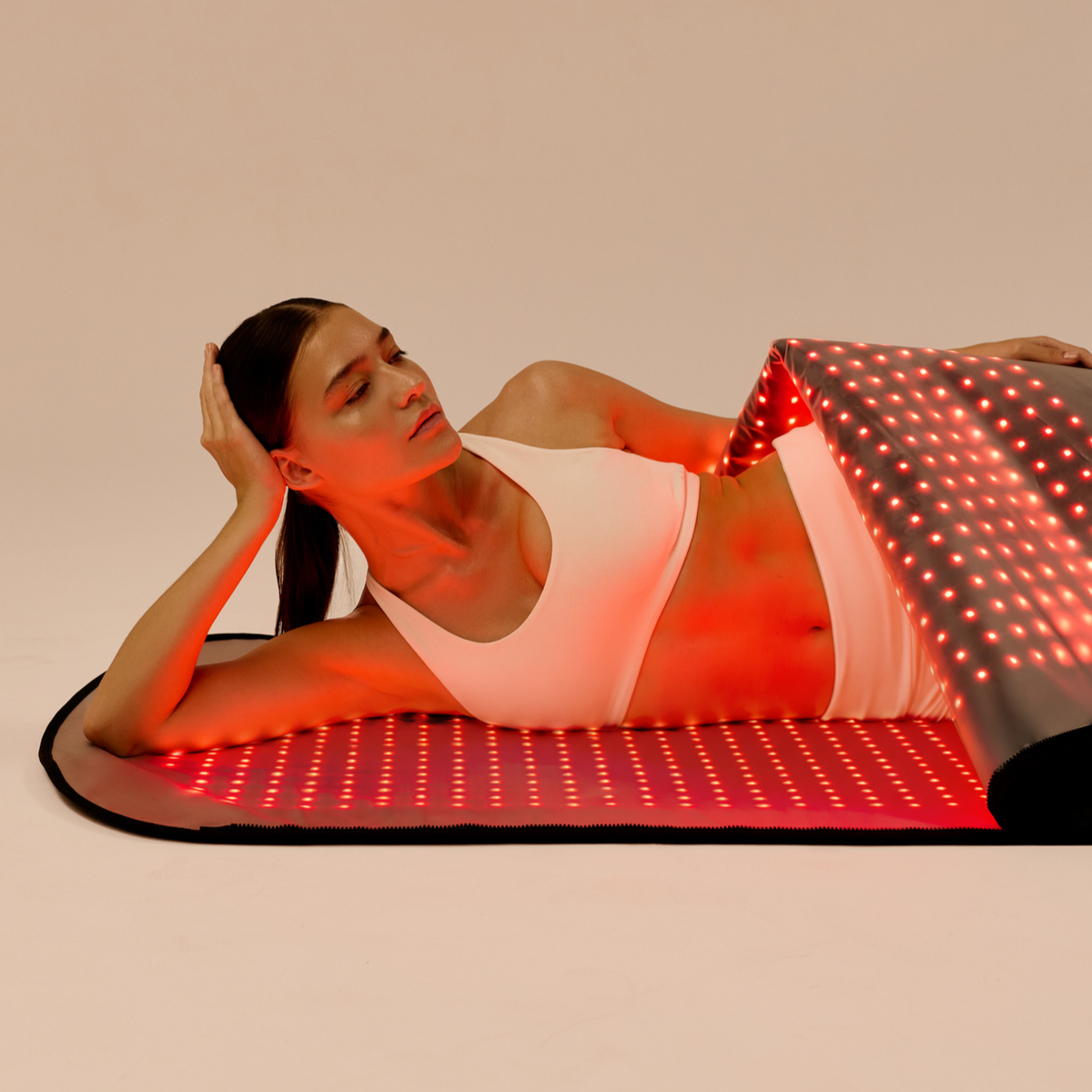 Femme allongée sur le tapis LED Restora+ inférieur allumé, soulevant le panneau supérieur